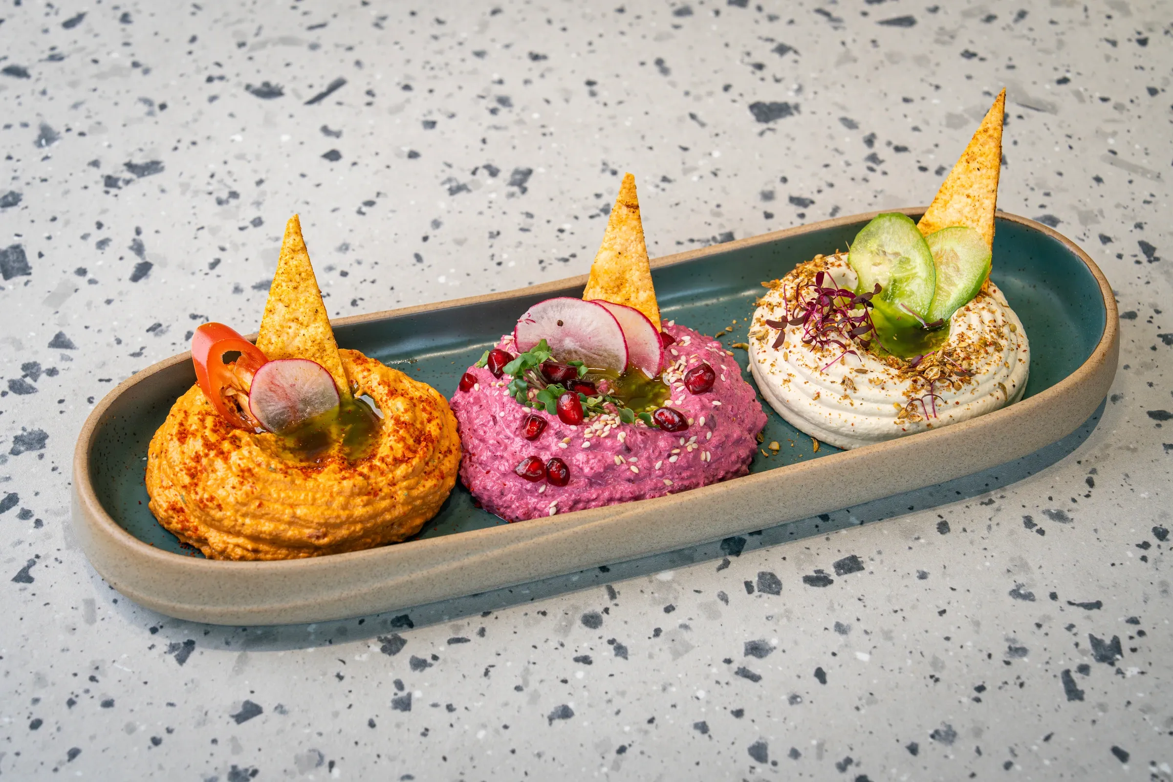 Three dips in a long oval dish: paprika-orange, beetroot and white with za’atar, each with a tortilla wedge